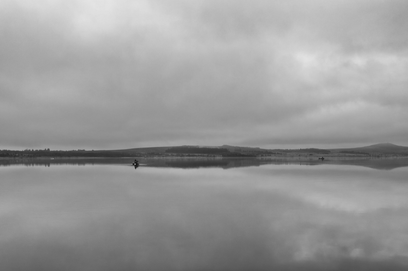 Deux barques minuscules posées sur un lac sans une ride, sous une ligne de collines basses. Le ciel se répète intégralement dans l'eau.
