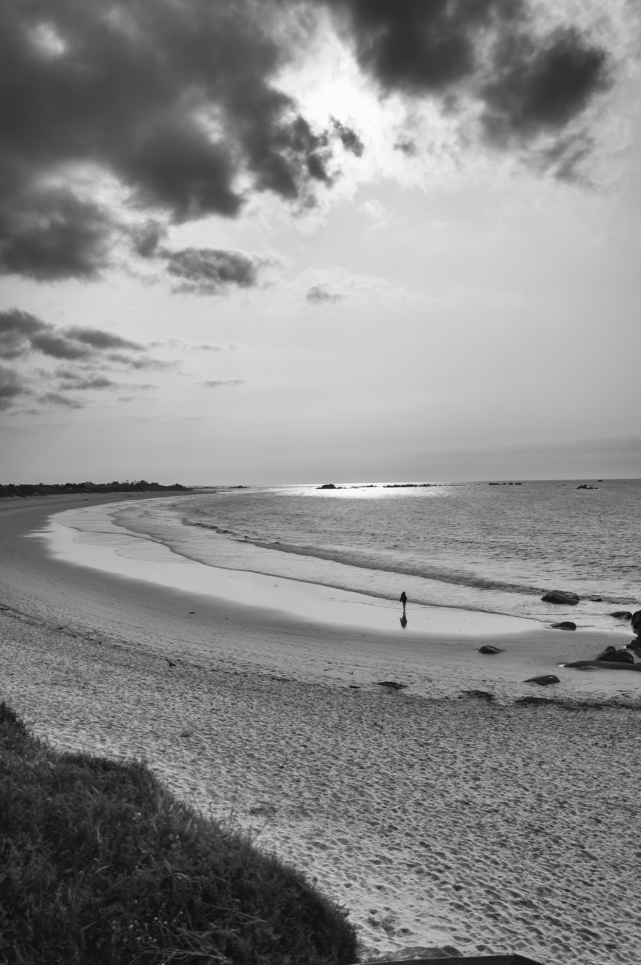 Une longue courbe de plage sous un ciel nuageux, quelques silhouettes minuscules au bord de l'eau.