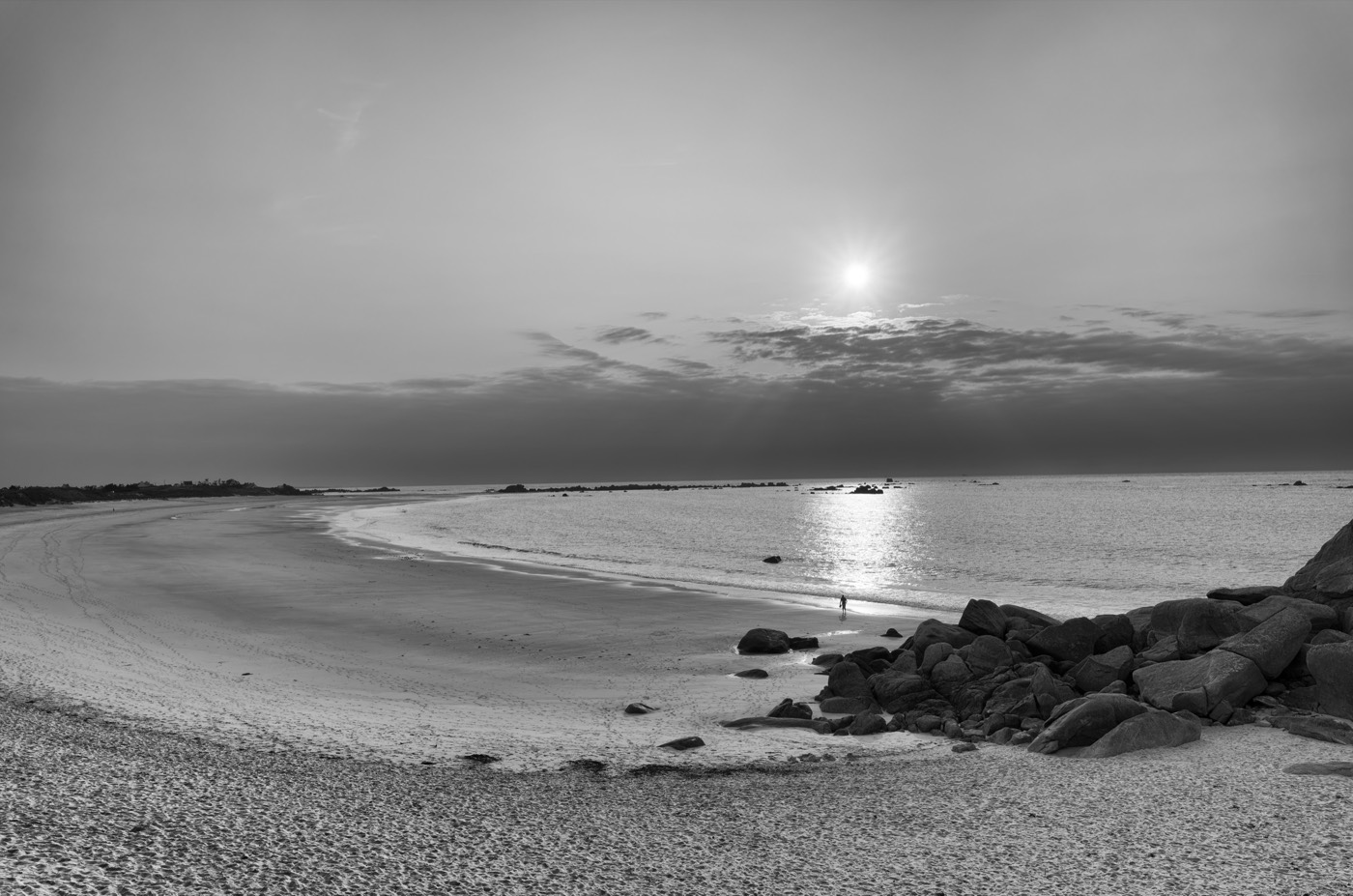 Vue large d'une baie au soleil bas, la trainée de lumière sur le sable mouillé, des silhouettes minuscules.