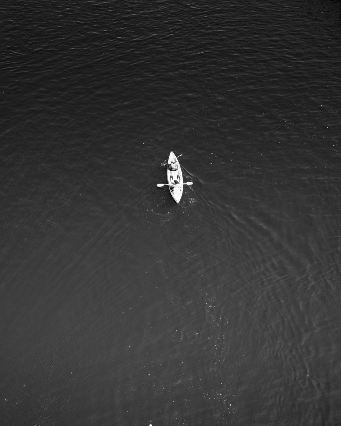 Deux silhouettes en canoë au milieu de l'eau, vues depuis l'aqueduc, un sillage de bulles derrière elles.