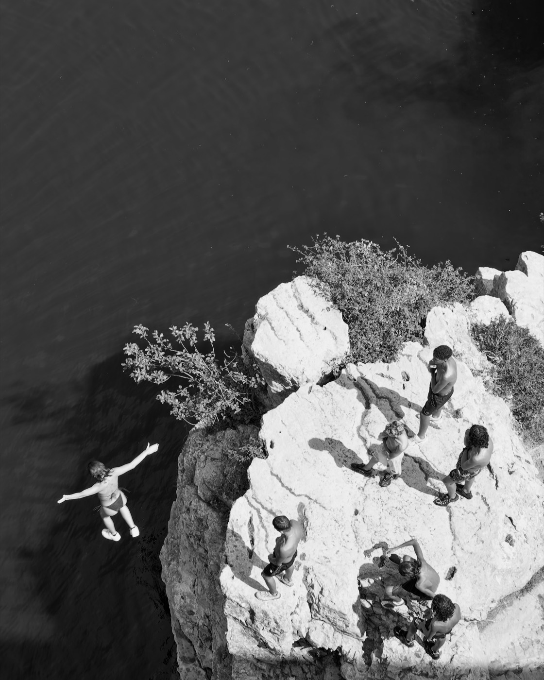 Une silhouette bras écartés, en suspension entre le rocher et l'eau.